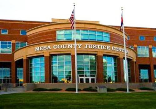 Photo of a red brick building with multiple, large windows and 2 flagpoles in front
