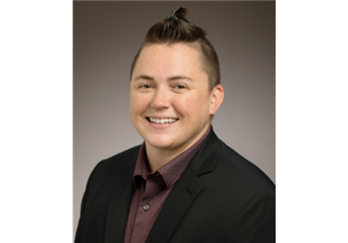 Photo of a white gender diverse person wearing a black blazer & maroon shirt