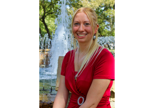 A young woman with long, blonde hair & wearing a red dress smiles