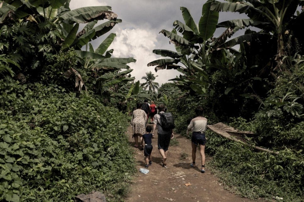 Several adults and a child walk the muddy path through tall, thick jungle; they face away from the camera