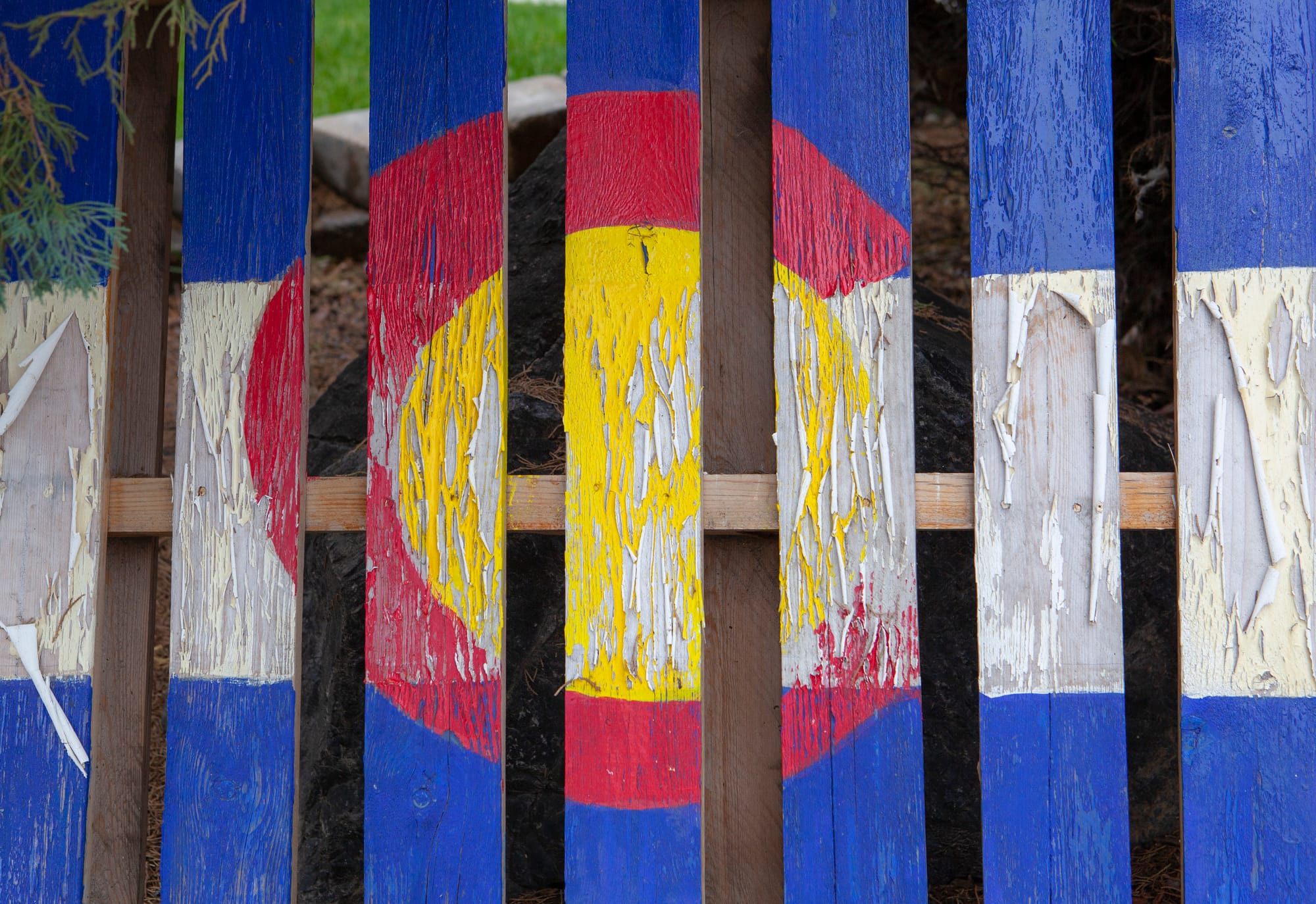 Fence with Colorado flag painted on it peeling away, fading and chipped in places
