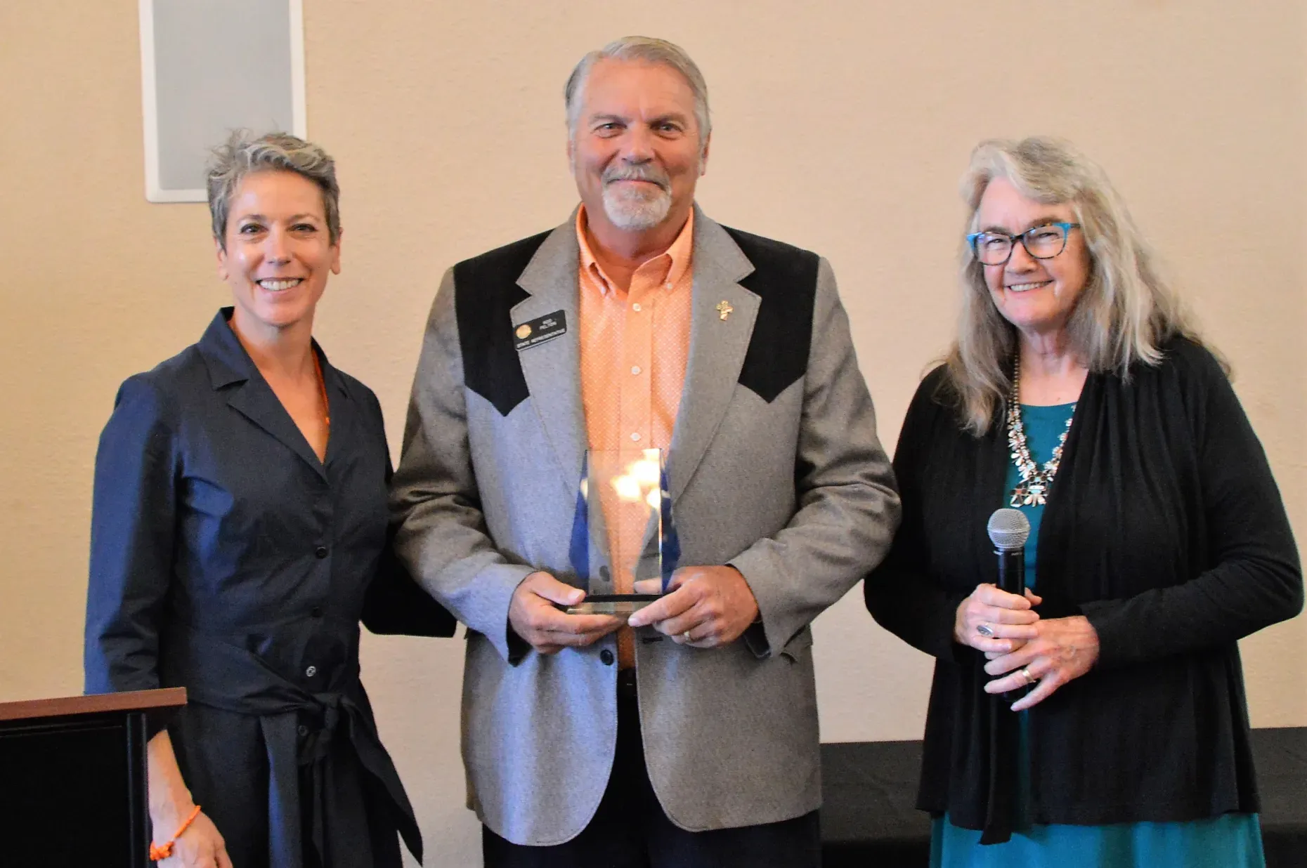 Photo of a man holding a glass award flanked by 2 women; all are smiling