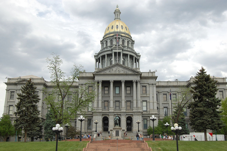 Photo of state capitol building w/gray facade and gold-leaf dome