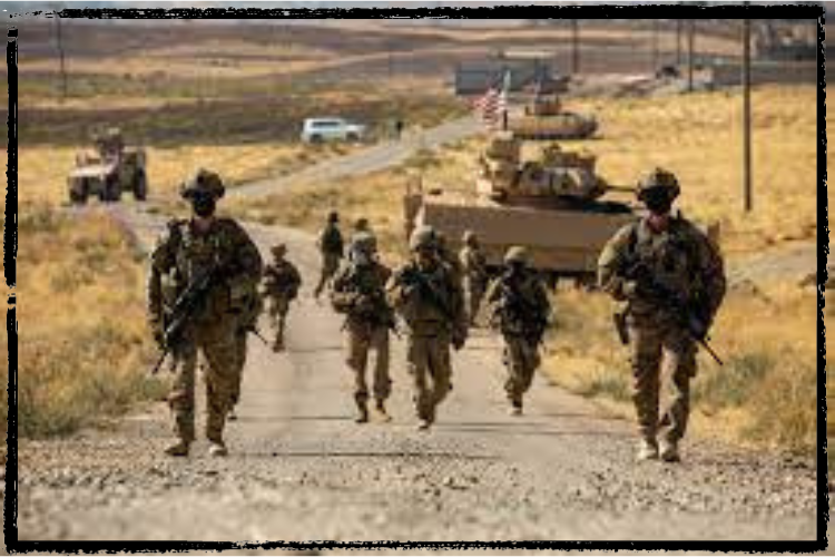 A group of armed soldiers walks down a gravel road with military vehicles in the distance