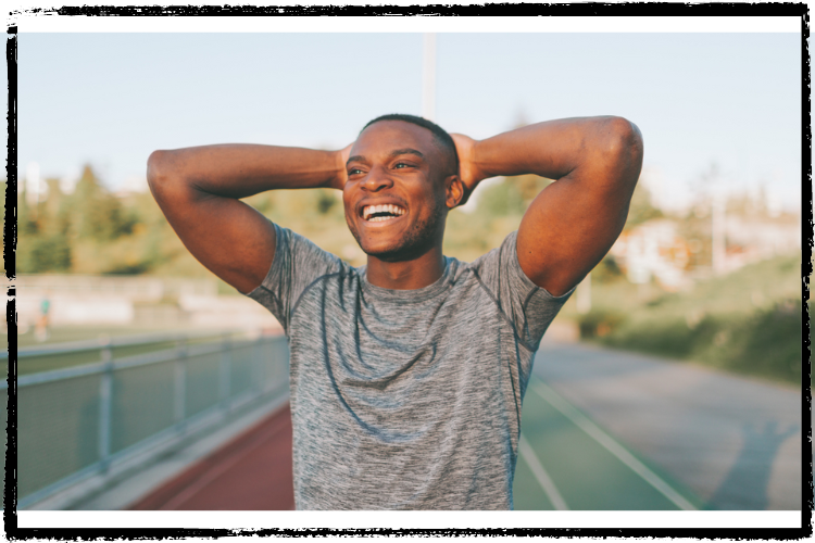 Photo of a young, Black men in a gray t-shirt grinning broadly after a run ona track