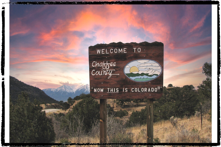 Photo: wood sign says, "Welcome to Chaffee County, Now this is Colorado" w/snow-covered mountain peaks behind