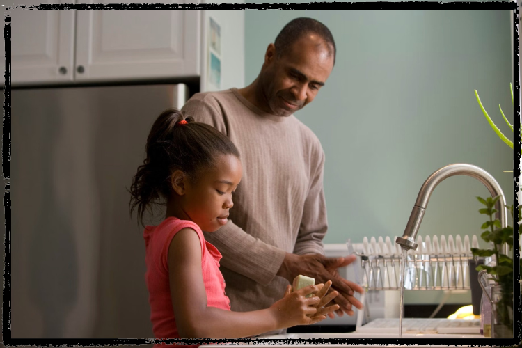A father washes his hands in the kitchen sink with his daughter