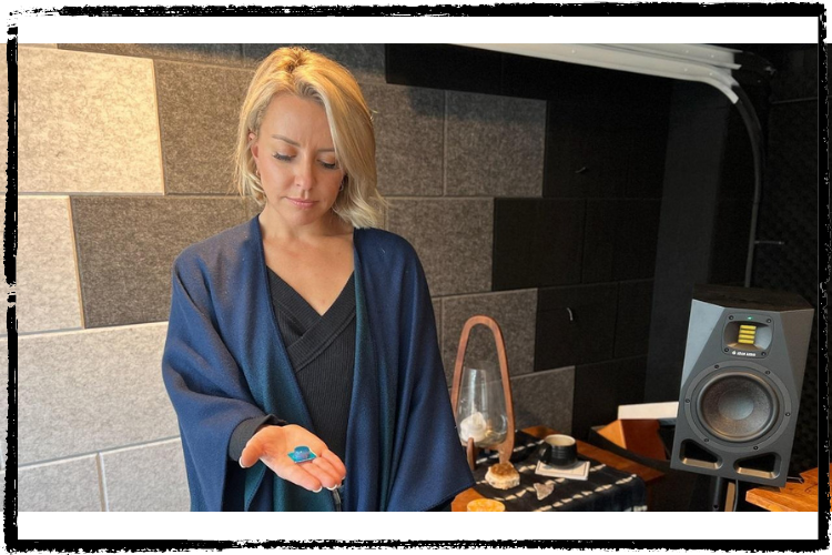 Photo of a woman w/short, blonde hair holding a large blue lozenge in her outstretched hand