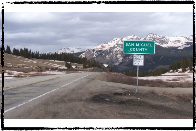 Photo of a green county sign framed by a snow-covered mountain range and forest