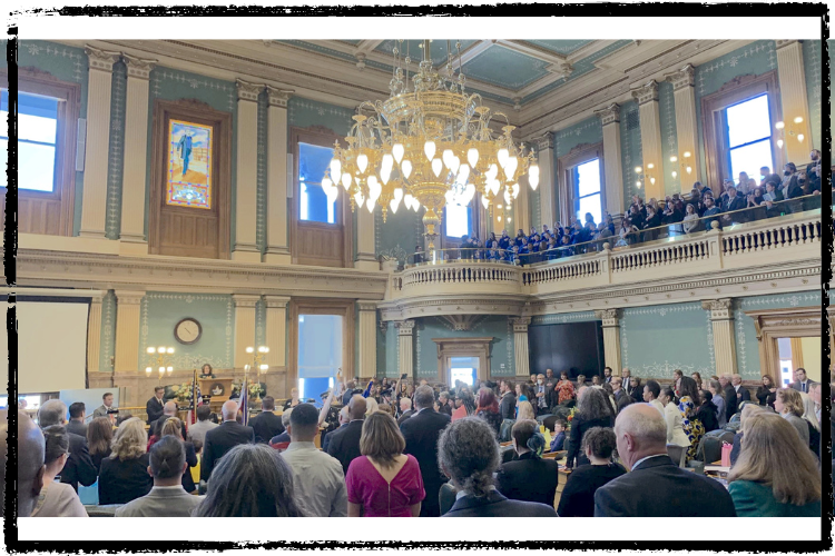 Photo of people gathered on the 1st floor and gallery looking at a woman standing at a podium in the front