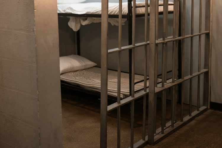 Photo of a jail cell with bunks. The sliding door is partly open