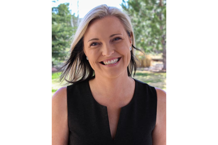 Photo of a white woman with shoulder-length blonde hair wearing a black, short-sleeve top