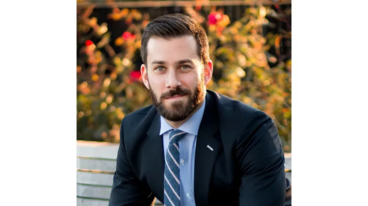 Photo of white man with brown hair and brown mustache & beard, dressed in a blue su