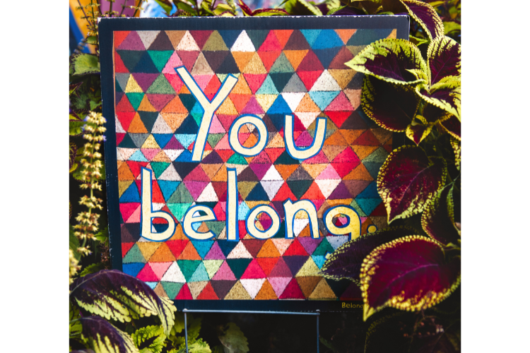 A multi-colored illustration, like a patchwork quilt, with the words "You belong" on it surrounded by plants.