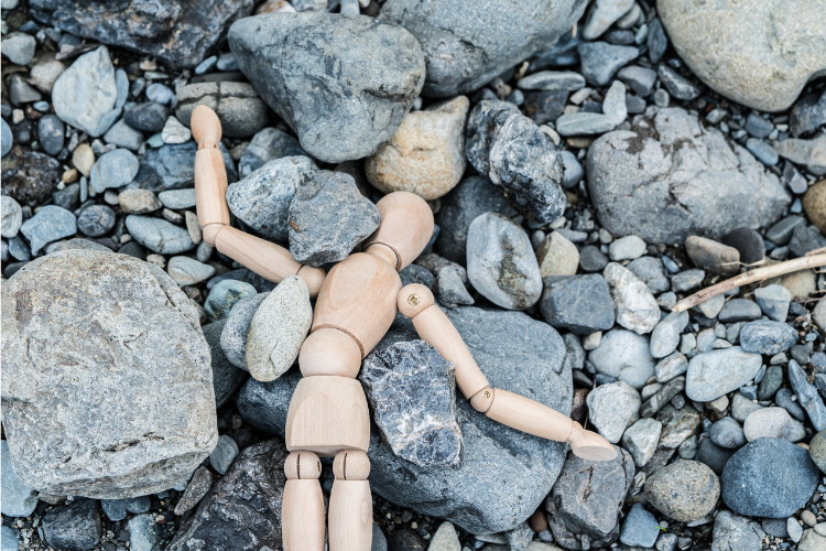 Photo of an artist's poseable, wood figure splayed on gray boulders