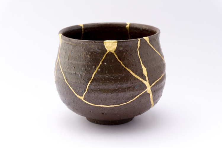 Photo of a brownish, pottery bowl traced with gold lines where the piece was mended