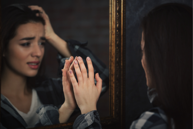 Photo of a young woman with olive skin & dark hair touches her reflection in a mirror 