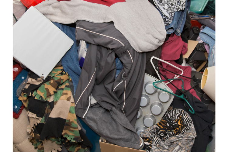 Many disparate items in a pile, including clothes, a muffin tin, hangers, a book, bags, a lampshafe