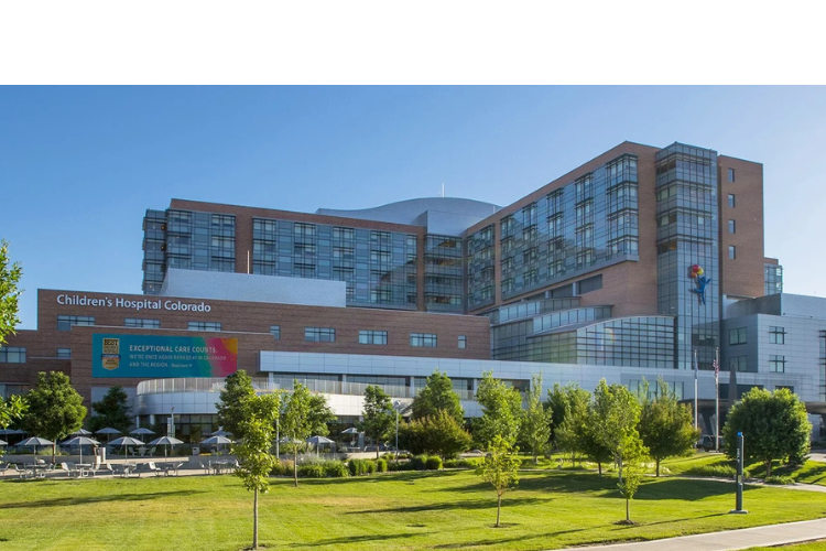 A large red brick and glass hospital with trees and grass in the foreground