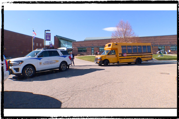 A school bus and police SUV are parked in front of a school in Larimer County