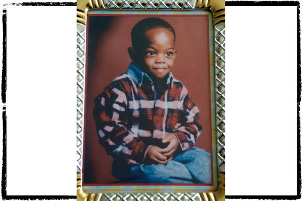 Photo of a small, Black boy wearing a plaid shirt and blue jeans