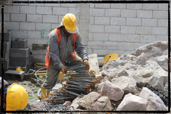 A construction worker leans on a stack of metal rebar w/his knee, surrounded by broken concrete