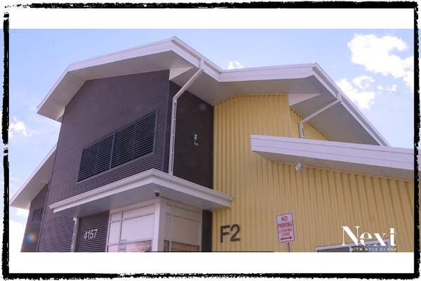 A 2-story building with a charcoal colored facade & yellow siding, all w/white eaves