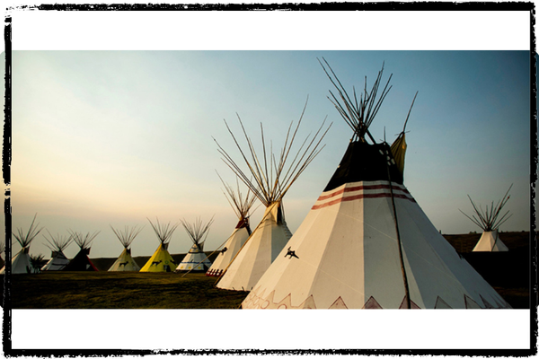 White tipis w/black animals painted on the sides and black tops w/red stripes dot the landscape