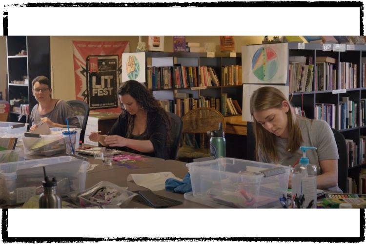 Photo of 3 white women at a long table working on personal art projects surrounded by art supplies and containers