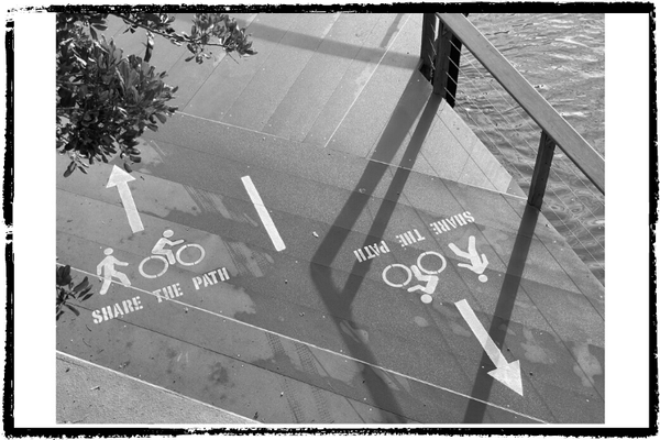 Photo of a 2-way bike & pedestrian on a platform near water. A painted stencil each way says, "Share the Path."