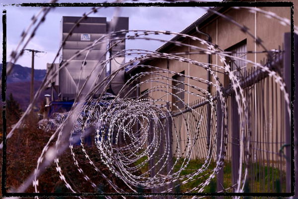 Photo of the top of a prison wall looking through spiraling razor wire running the length of it