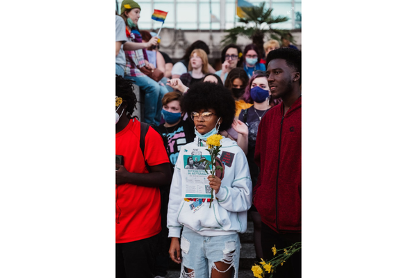 Photo of diverse youth on a college campus waving Pride flags and holding flowers