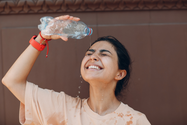 A young Woman of Color pours a plastic bottle of water on her face