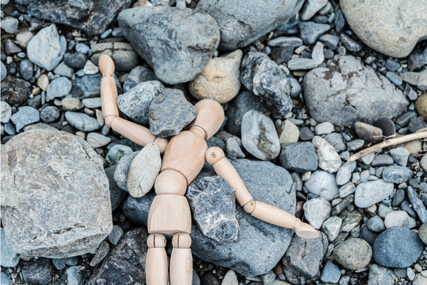Photo of an artist's poseable, wood figure splayed on gray boulders