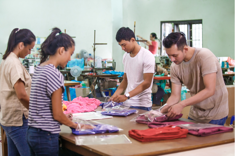 Photo of 2 women & 2 men with Asian features work at a table folding clothes into bags