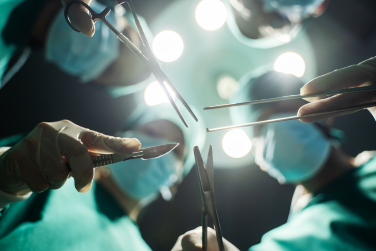 Photo looking up at masked surgical staff holding various instruments with bright lights behind