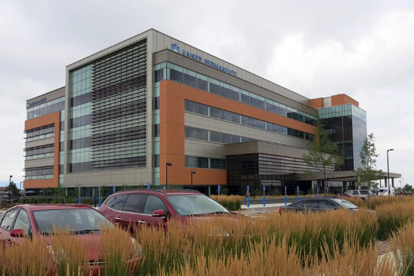 A 5-story, red brick and glass building with cars in the parking lot